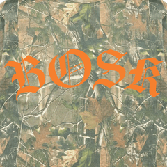 The BOSK Camo Tee features a forest-like, camouflage background with leaves and branches. The brand name "BOSK" is boldly showcased in large, orange, Gothic-style letters across the center for a striking contrast.