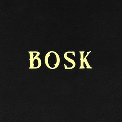 The image features "BOSK" in bold, yellow, uppercase serif letters centered on a black background, reflecting the graphic on BOSK's Allure LS Tee—a classic long sleeve t-shirt made from heavy-weight cotton with a vintage or gothic style.