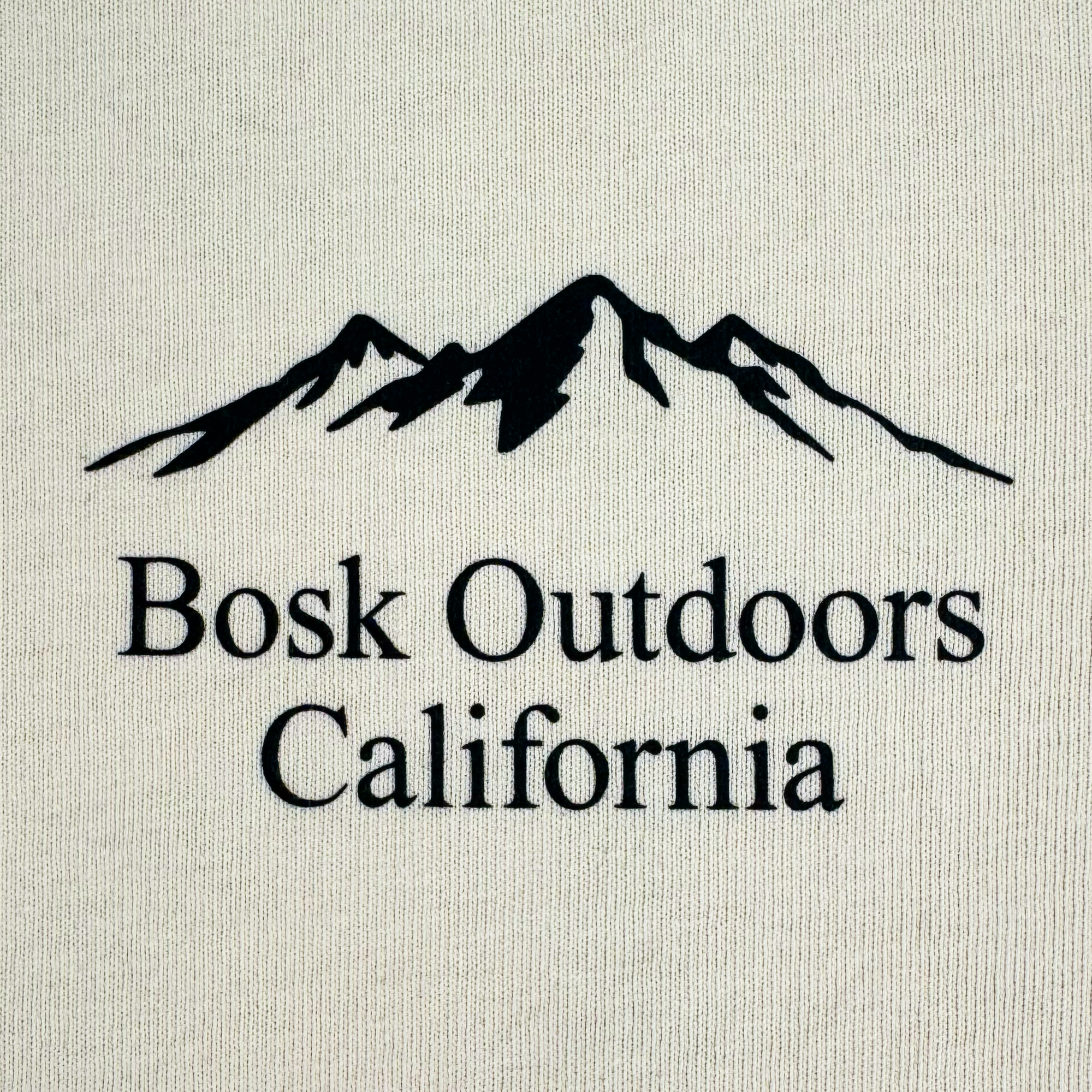 The Bosk Outdoors Tee by BOSK showcases a stylized black silhouette of a mountain range above bold black "Bosk Outdoors California" text on a light beige backdrop, evoking an outdoor adventure feel.