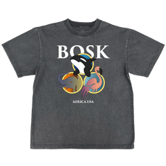 The BOSK World Tee is a classic fit, heavy-weight faded black t-shirt featuring bold white "BOSK" lettering above cartoon orca, elephant, and flamingo in colorful circles and "AFRICA USA" underneath for a casual, worn look.